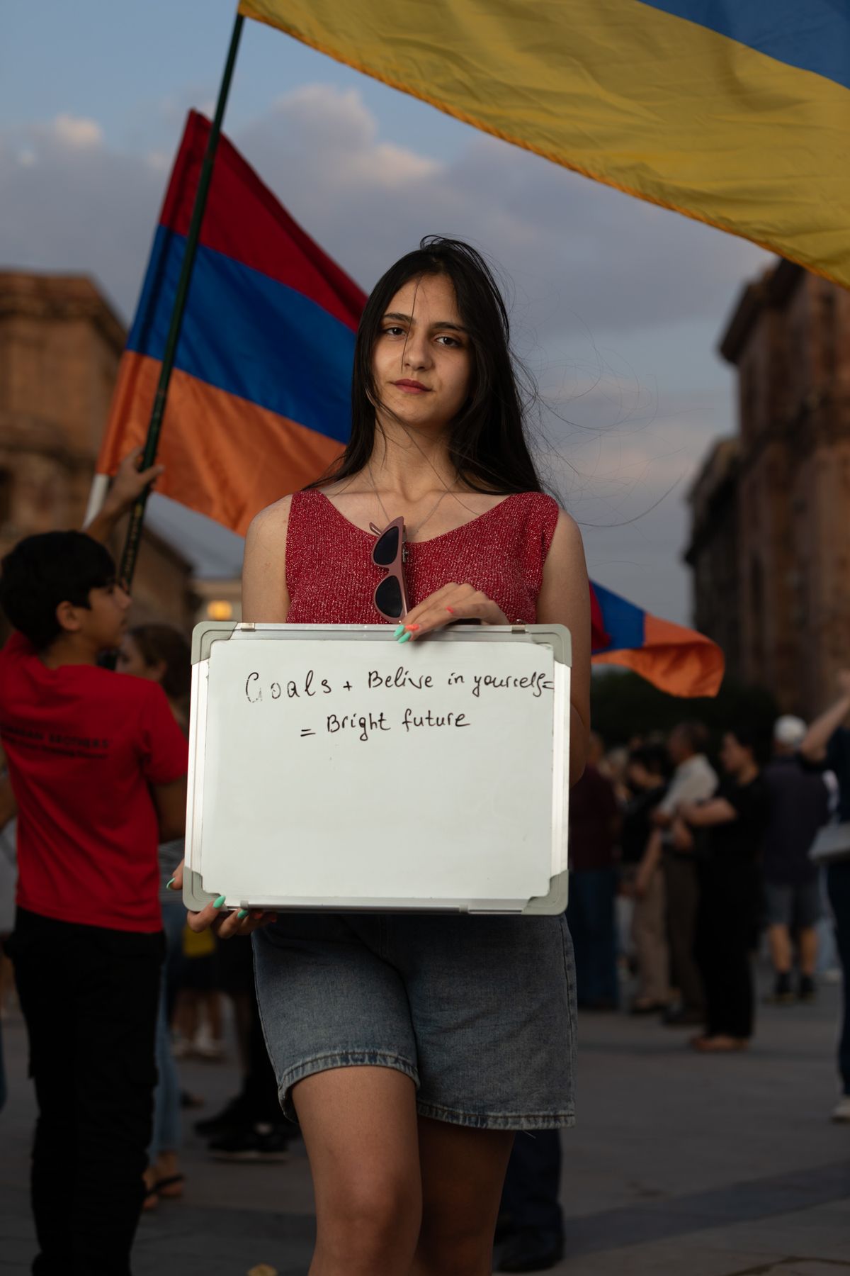 A young woman holds a whiteboard under Armenian flags