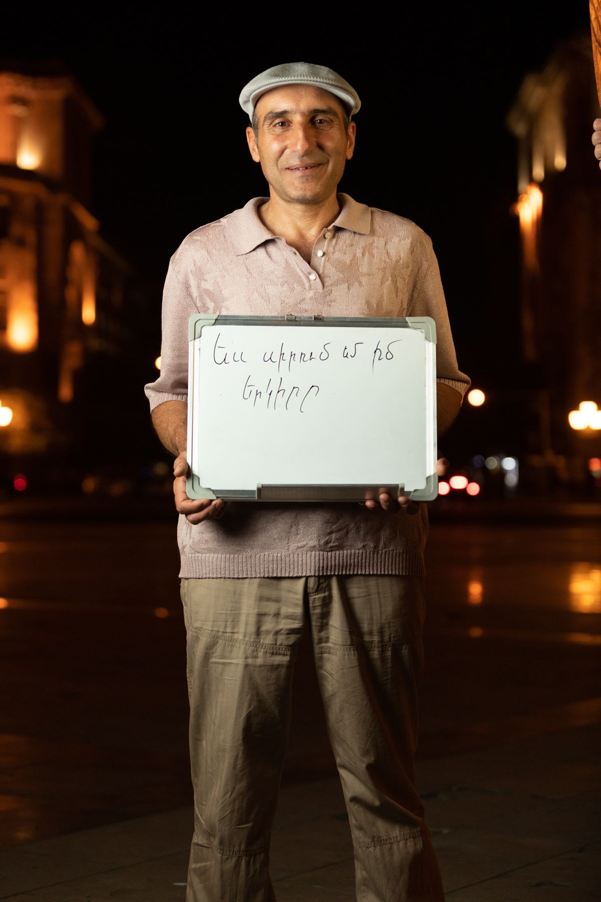 An older man holds a whiteboard in the square at night