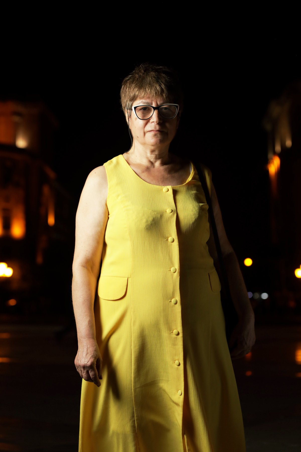 A woman in a yellow dress stands in the square at night