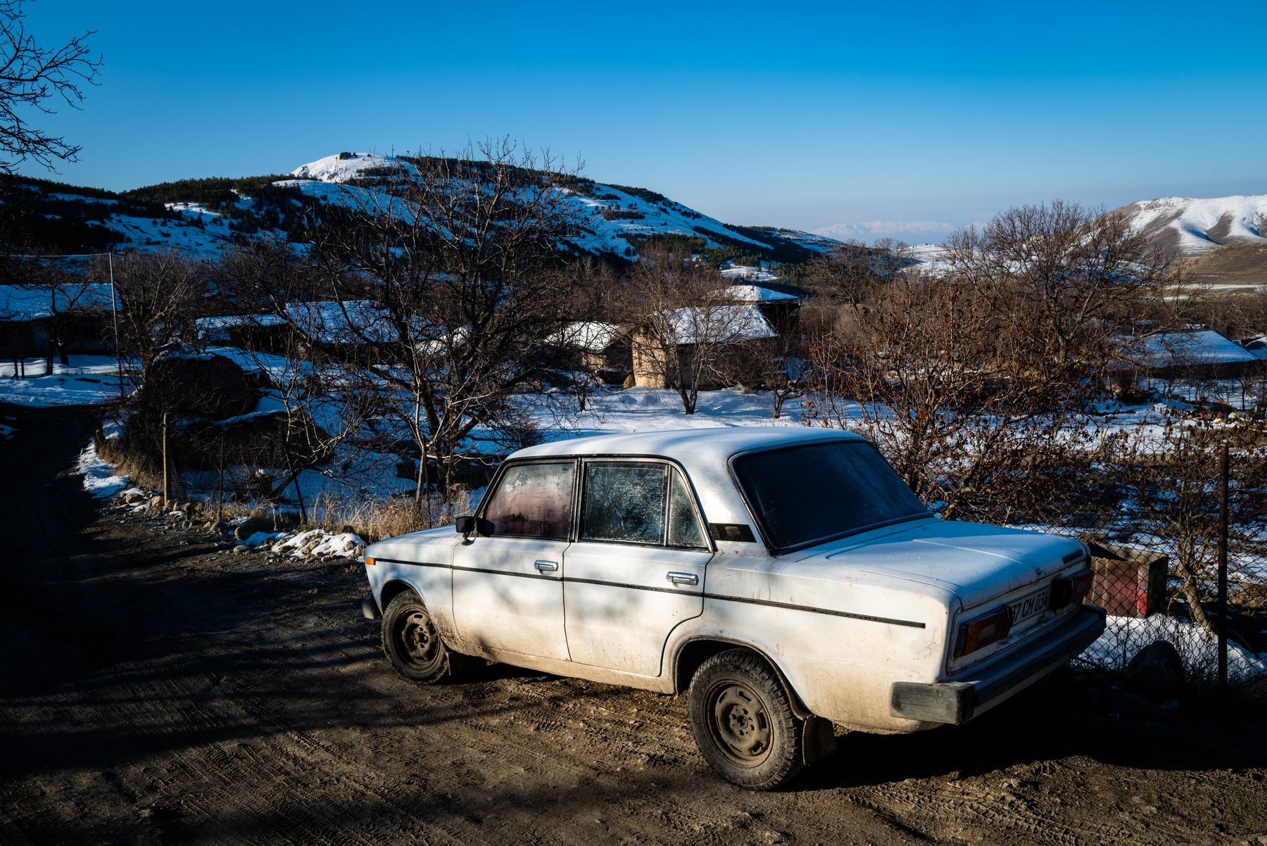 A white Lada parked on a snowy slope, with mountains behind