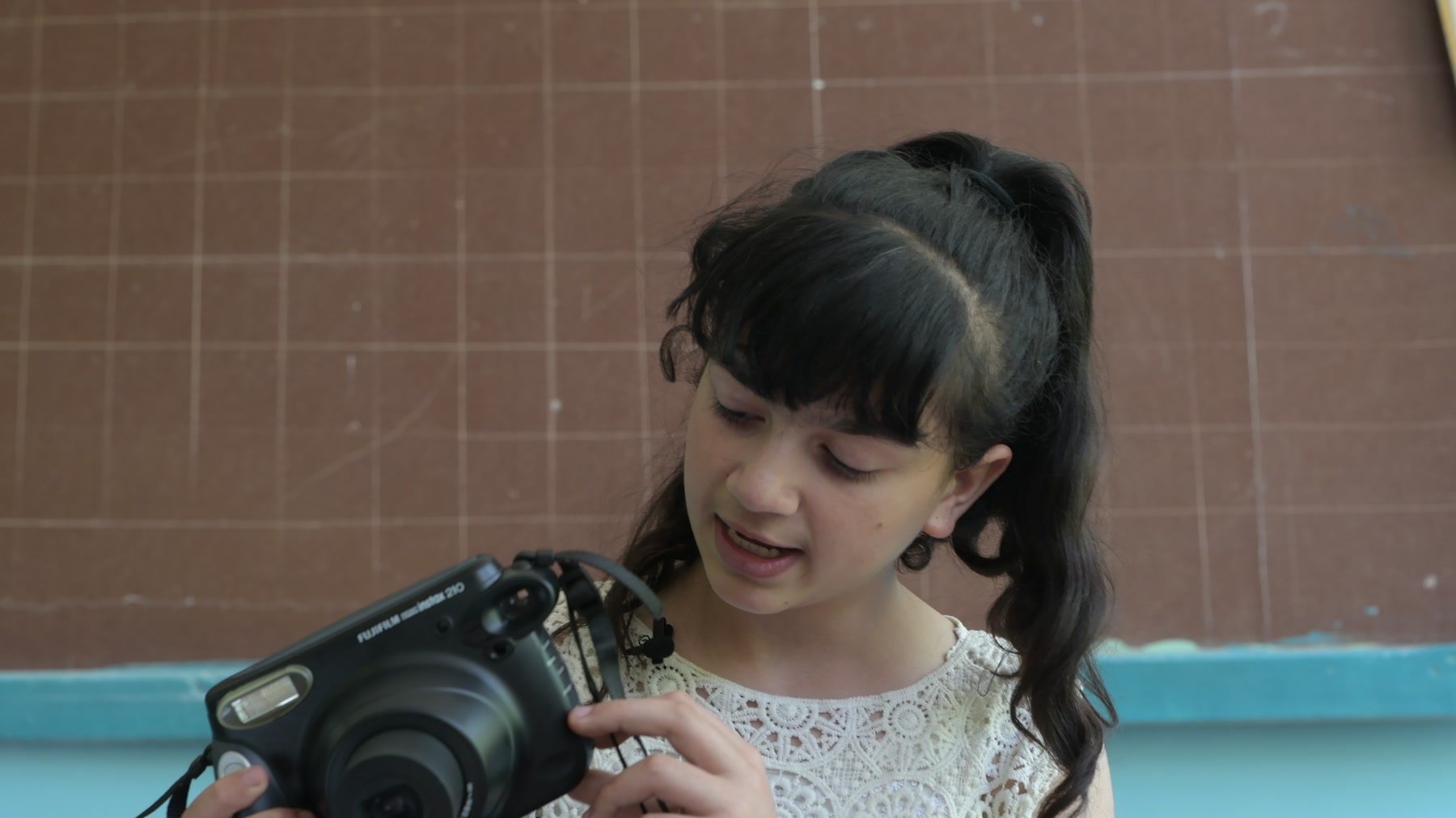 A girl with dark plaits looks down at the Instax camera in her hands