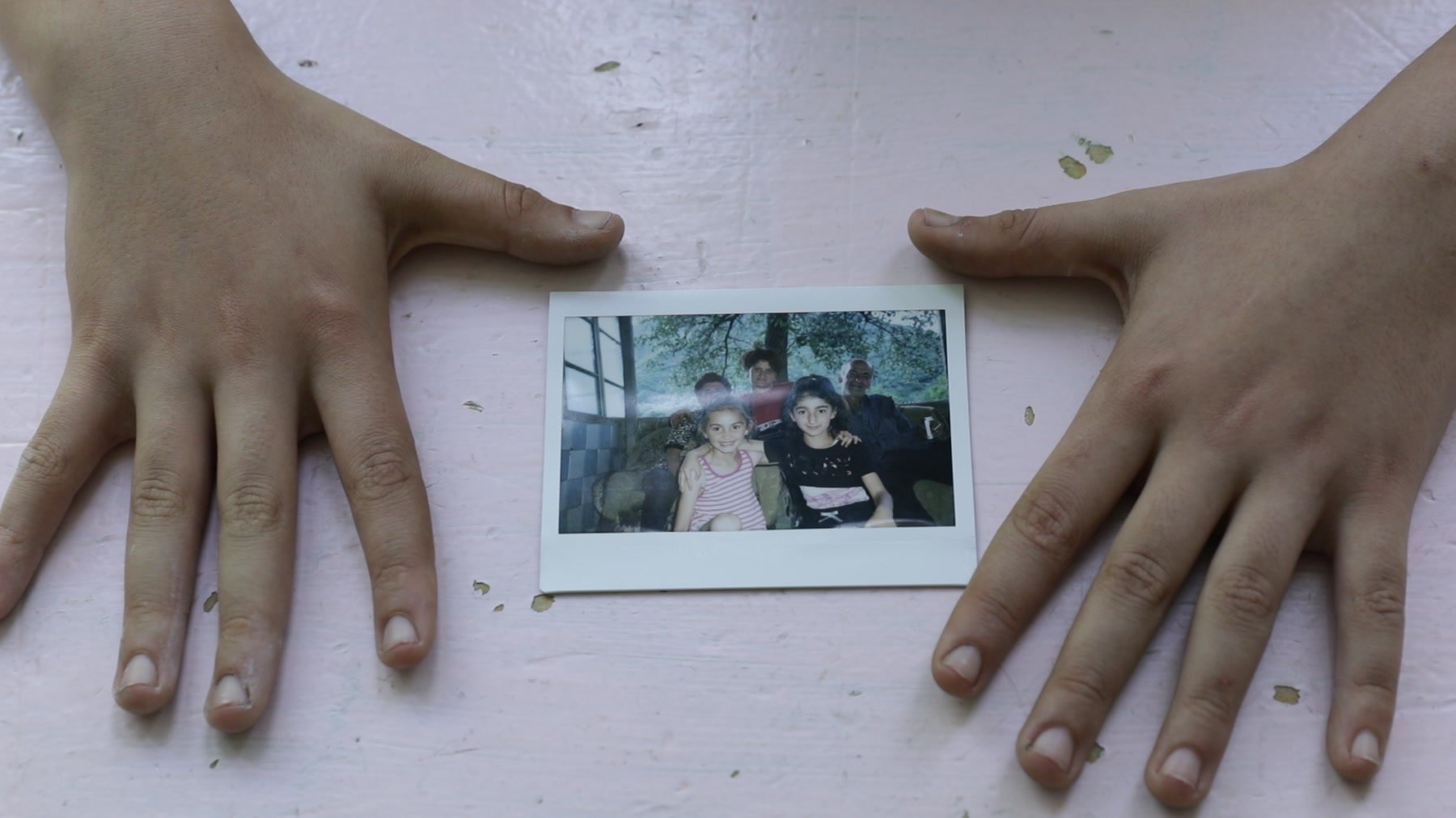 Two hands frame an instant print of a family on pink paper
