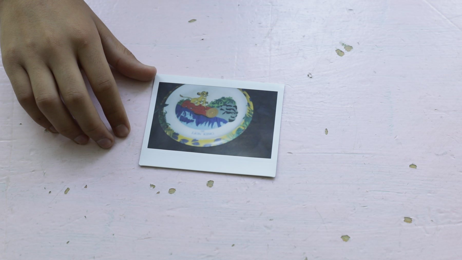 A hand sets down an instant print of a painted plate