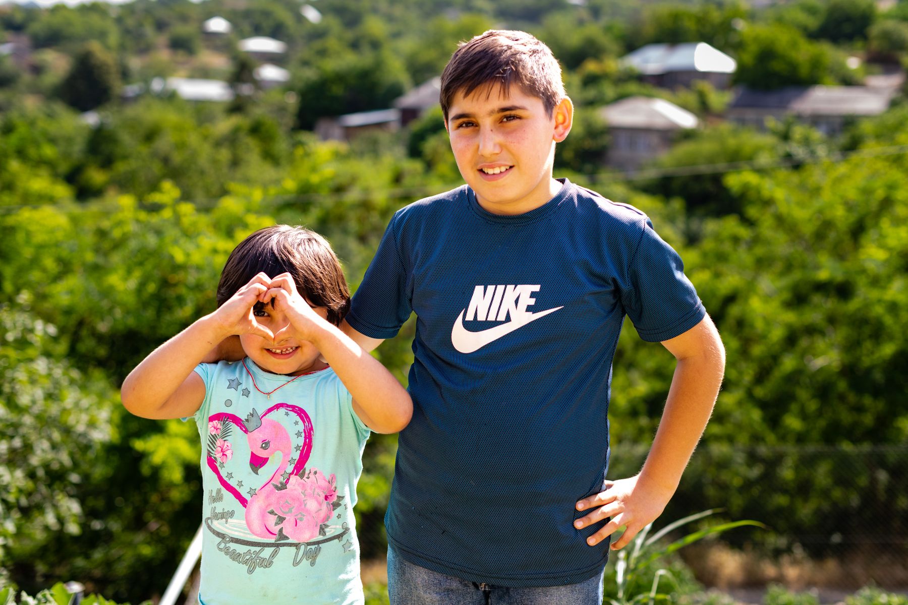 A girl makes a heart with her hands beside an older boy