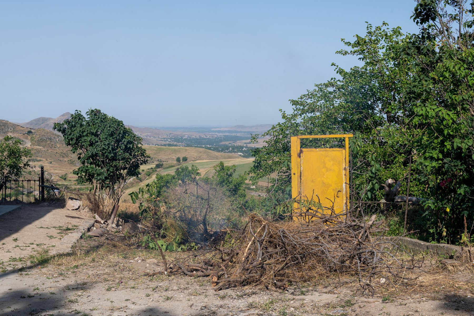 A yellow door among bushes on a hillside, a plain beyond