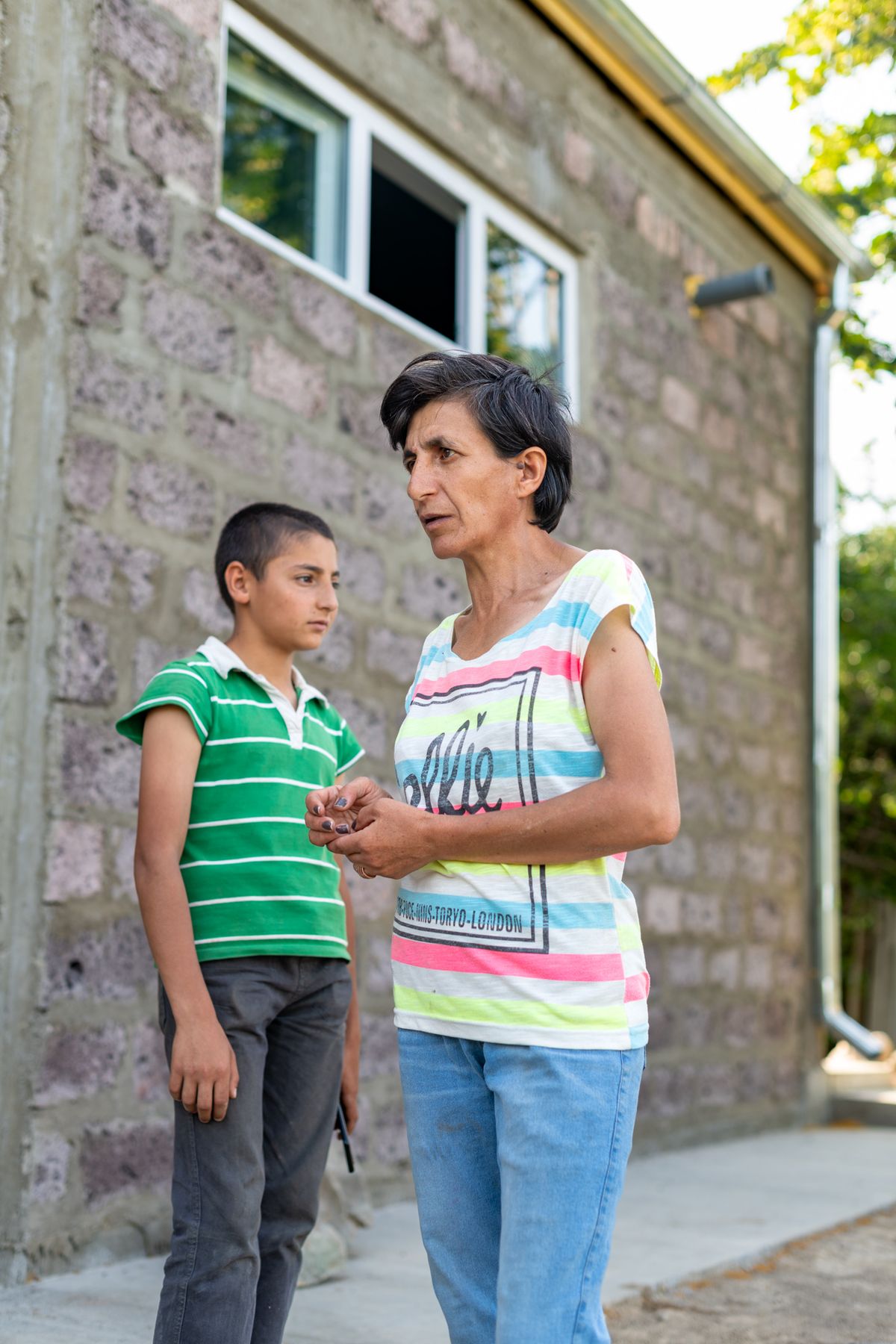 A mother and her son talk outside a stone house