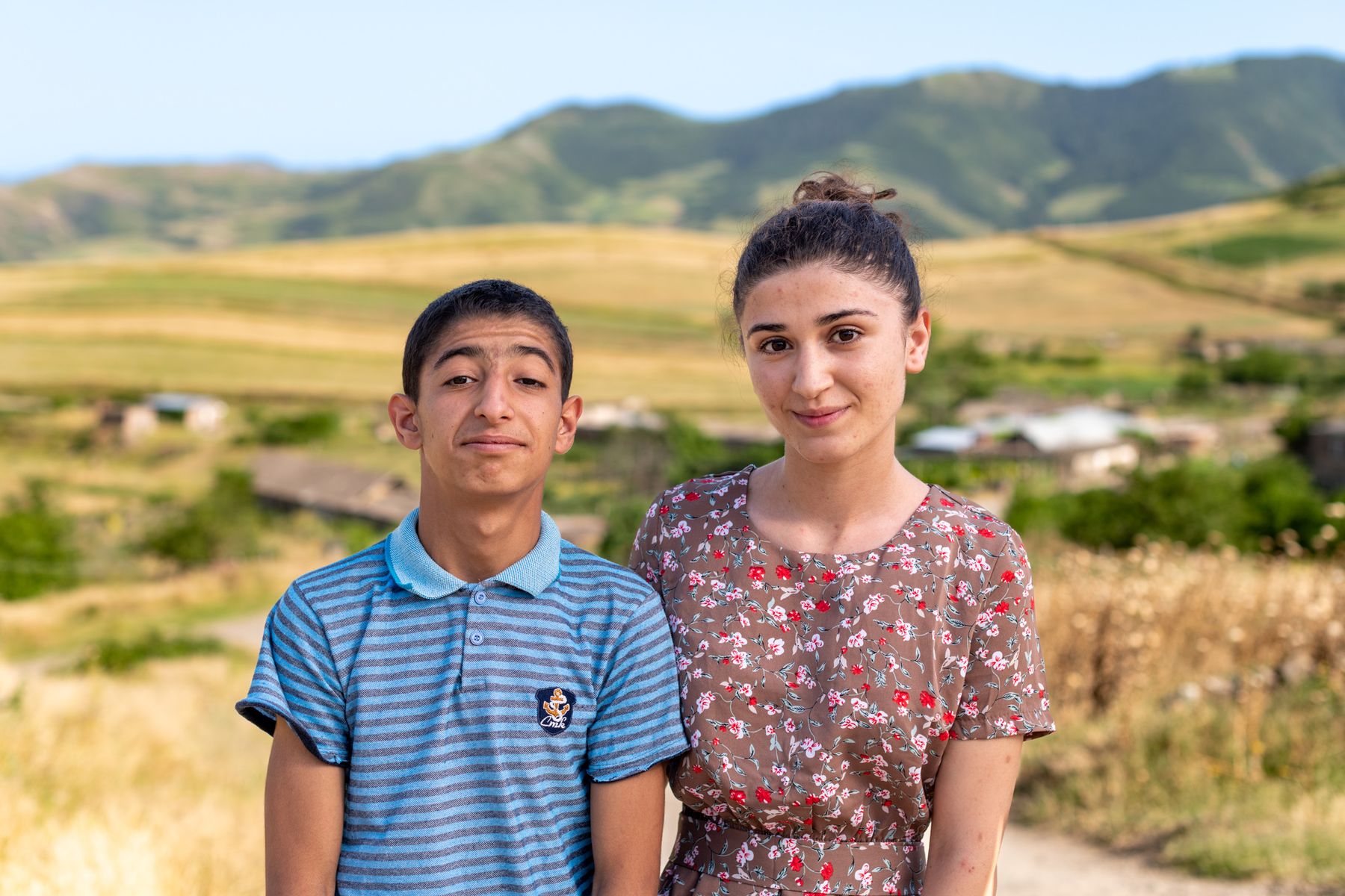 A boy and a young woman stand in front of the hills